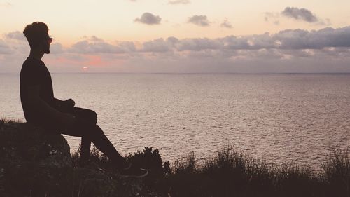 Side view of man looking at sea against sky during sunset