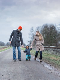 Full length of family walking on road against sky during winter