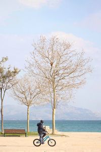 Side view of man riding bicycle at beach against sky