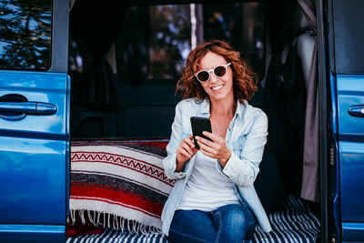 Woman wearing sunglasses using mobile phone in camper trailer