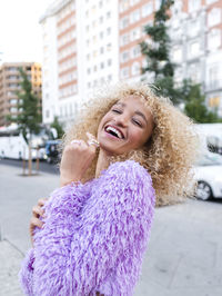 Happy young woman laughing on footpath in city