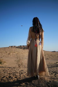 Woman standing on sand dune in desert against sky