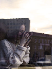 Side view of woman drinking coffee while reflecting on window