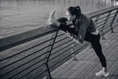 Side view of woman exercising on pier over river