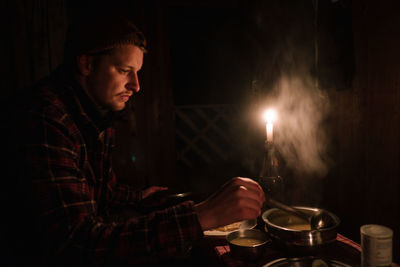 Young man eating food while sitting in darkroom