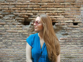 Beautiful young woman standing against brick wall