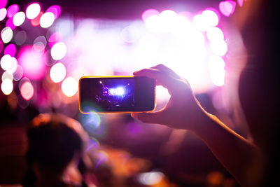 Cropped hands recording music concert through mobile phone at night