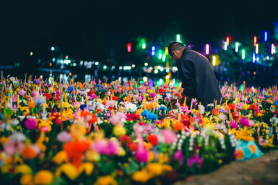 Rear view of man standing by flowering plants at night