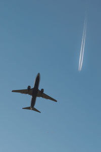 Low angle view of airplane flying against clear blue sky