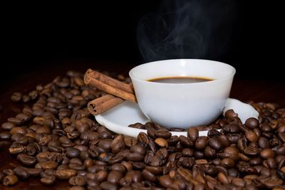 Close-up of coffee cup with roasted beans and cinnamon on table