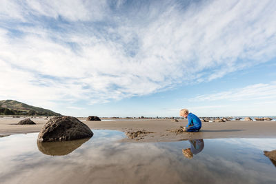 Boy playing in sand at beach with blue sky and reflection