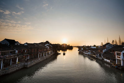 River amidst buildings against sky during sunset