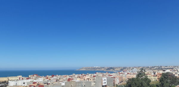 Aerial view of townscape by sea against clear blue sky