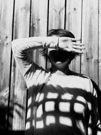 Woman covering face while standing against wall in sunny day