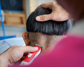 Asian child getting haircut at home from the father. young boy save his head using electric razor.