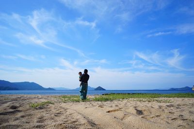 Rear view of man walking with baby on sand at beach against sky