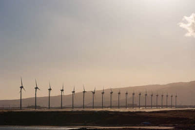 Windmills on landscape against sky during sunset