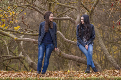 Happy friends standing against trees in forest during autumn