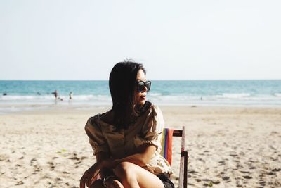 Woman sitting on chair beach against clear sky