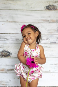 Smiling girl holding pink flower against wooden wall