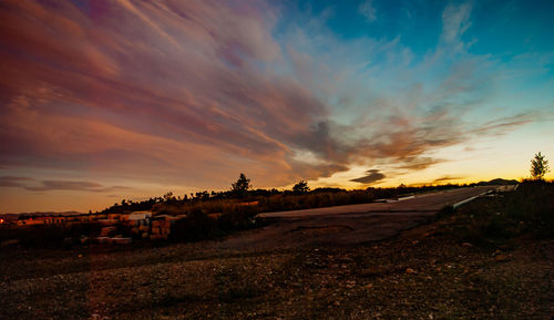 Road amidst field against sky during sunset