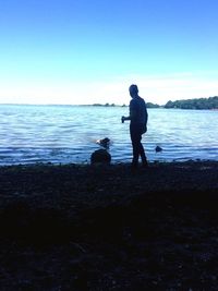 Rear view of father and dog on beach against clear sky
