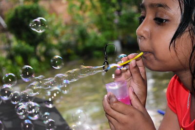 Side view of girl blowing bubbles while standing outdoors