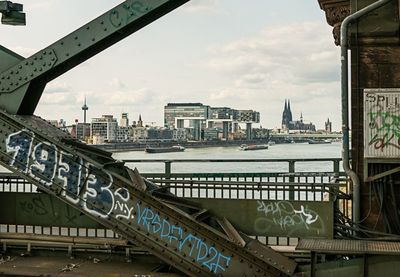 Bridge over river by buildings in city against sky