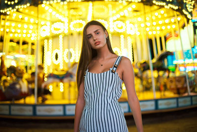 Young woman looking away while standing on illuminated street at night