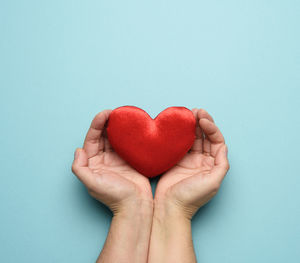 Cropped image of hand holding heart shape over turquoise background