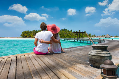 Rear view of couple sitting on pier against sky