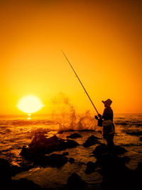 Silhouette man fishing in sea against sunset sky