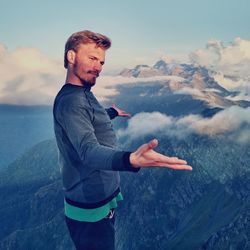 Young man with arms outstretched standing on mountain against sky