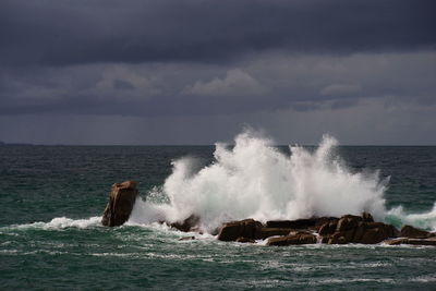 Waves splashing on rocks against sky