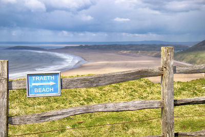 Information sign by fence on landscape against sky