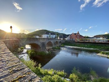 Arch bridge over river by buildings against sky