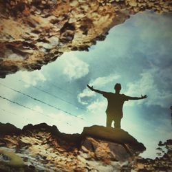 Low angle view of man standing on rock against sky