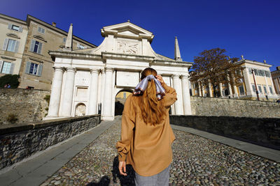 Young tourist woman walking towards bergamo porta san giacomo gate, bergamo, italy