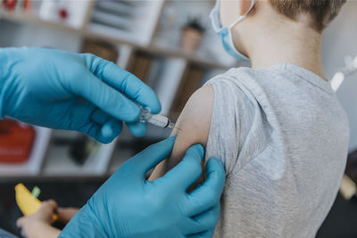 Doctor wearing protective glove injecting covid-19 vaccine in boy arm at clinic