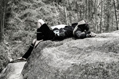 Woman sleeping on rock against trees in forest