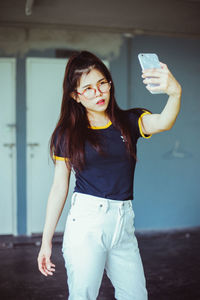 Portrait of smiling young woman standing against wall