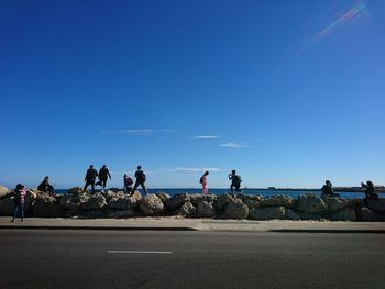 People walking on rocks by sea against blue sky