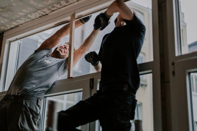 Two young workers are sealing cracks with tape on a window frame. person