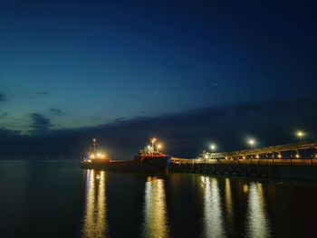 Illuminated pier over sea against sky at night