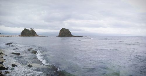 Scenic view of sea and rocks against cloudy sky