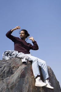 Low angle view of man sitting on rock against sky