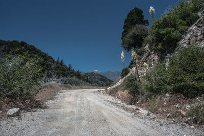 Dirt road by mountain against clear sky