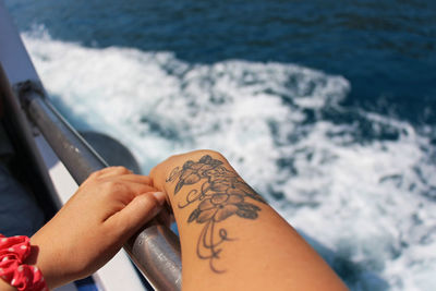 Midsection of woman with tattoo on hand at sea shore