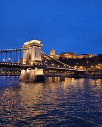 Illuminated bridge over river against sky at night