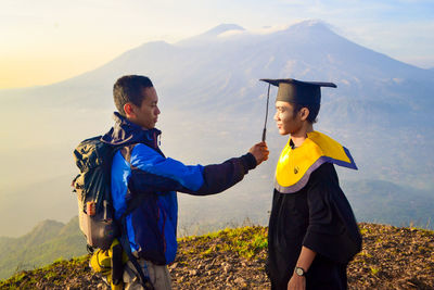 Side view of backpacker holding student mortarboard on mountain